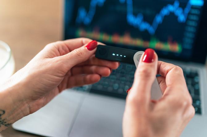 A person holding a cryptocurrency digital wallet in front of a laptop